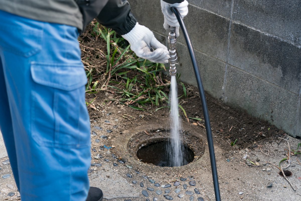 屋外の排水桝にホースを入れて高圧洗浄している様子